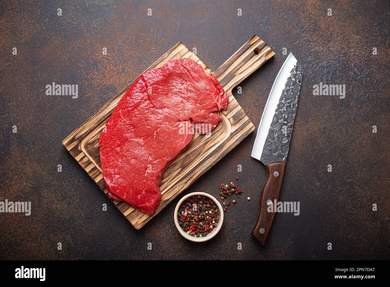 https://c8.alamy.com/comp/2PN7DAT/raw-uncooked-top-round-beef-steak-on-wooden-cutting-board-with-big-kitchen-knife-and-pepper-on-dark-brown-rustic-stone-background-top-view-cooking-2PN7DAT.jpg