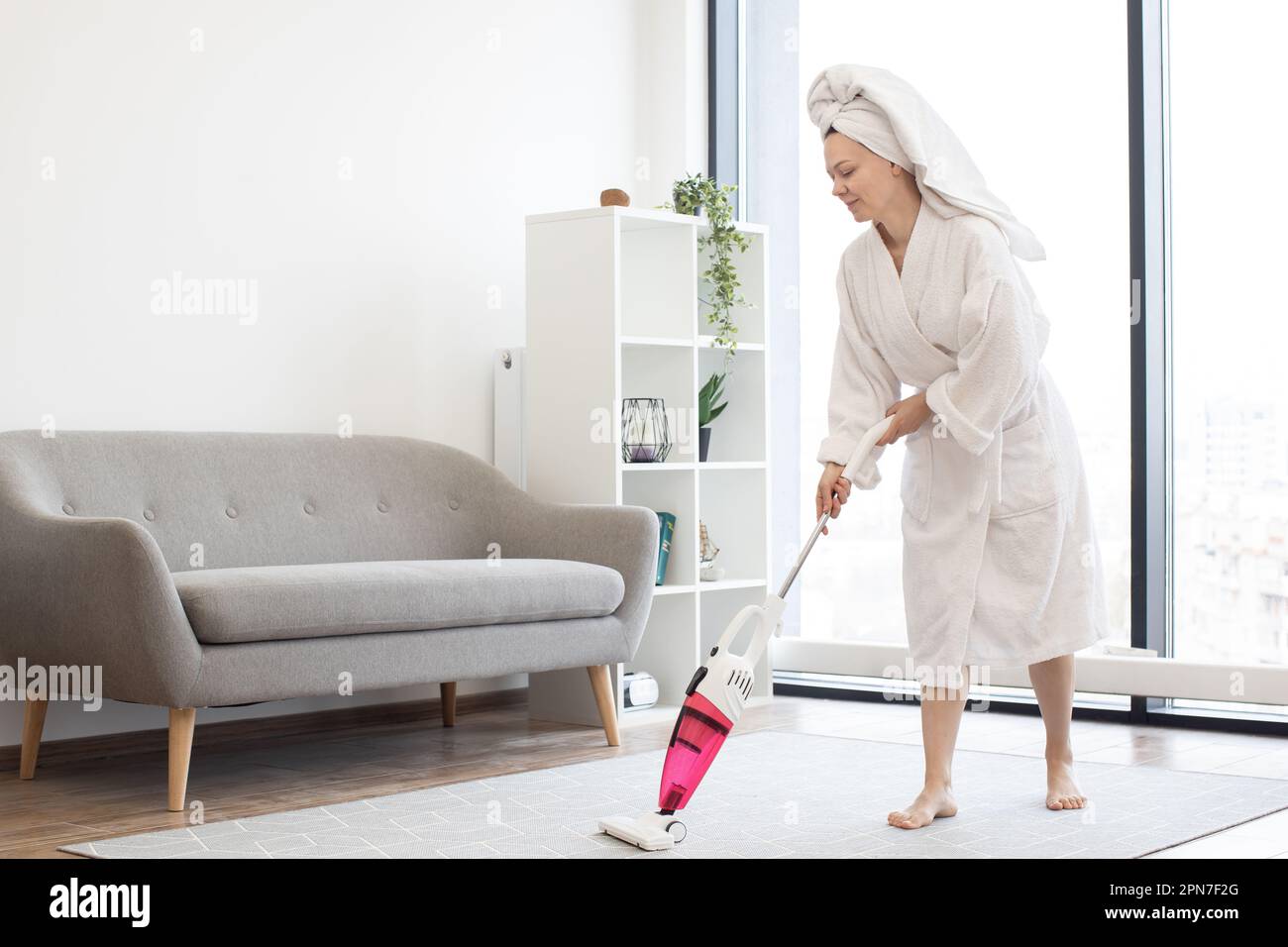Young woman in bathrobe and towel on head removing dust from soft ...