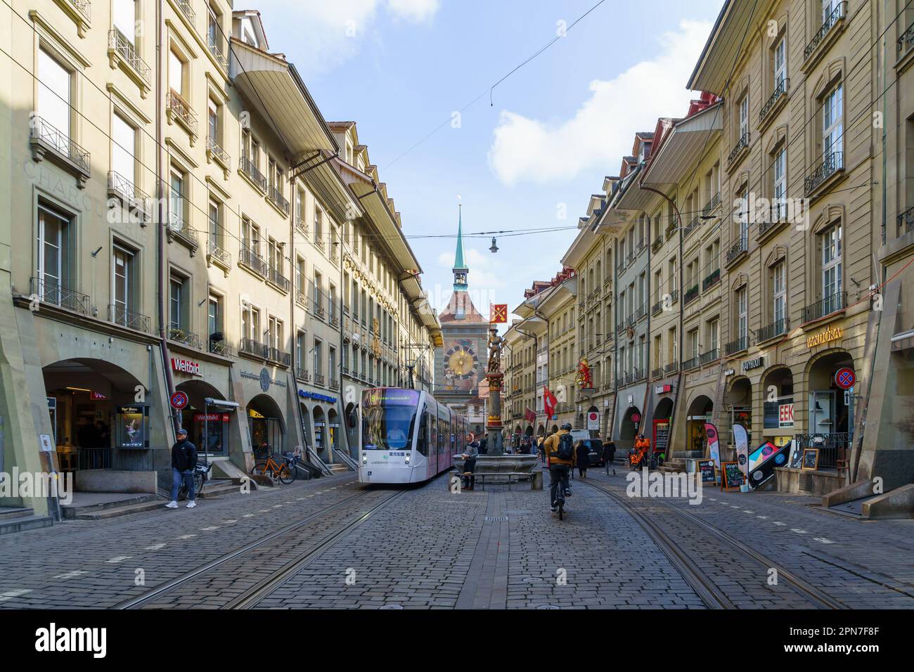 Bern, Switzerland - February 23, 2023: View of the marktgasse street, with tram, the Schuzenbrunnen fountain, Zytglogge clock tower, locals, and visit Stock Photo
