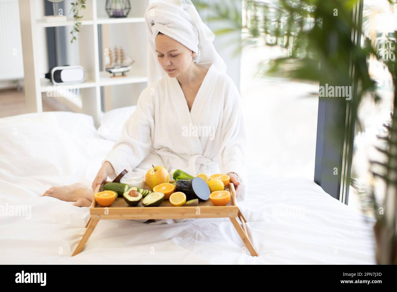 https://c8.alamy.com/comp/2PN7J3D/beautiful-young-lady-in-dressing-gown-putting-tray-table-with-fruits-and-cosmetic-containers-on-soft-bed-in-bright-studio-room-caucasian-woman-preparing-for-skin-care-treatment-during-home-spa-day-2PN7J3D.jpg