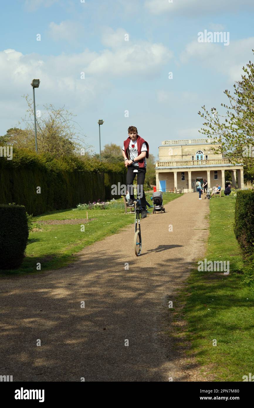 Young man pedalling a giraffe unicycle in Waterloo Park, Norwich, UK Stock Photo
