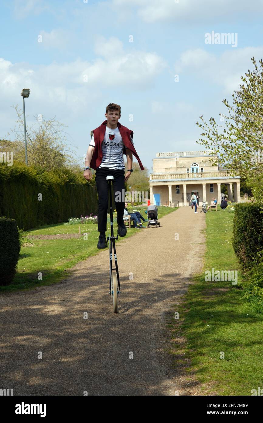 Young man pedalling a giraffe unicycle in Waterloo Park, Norwich, UK Stock Photo