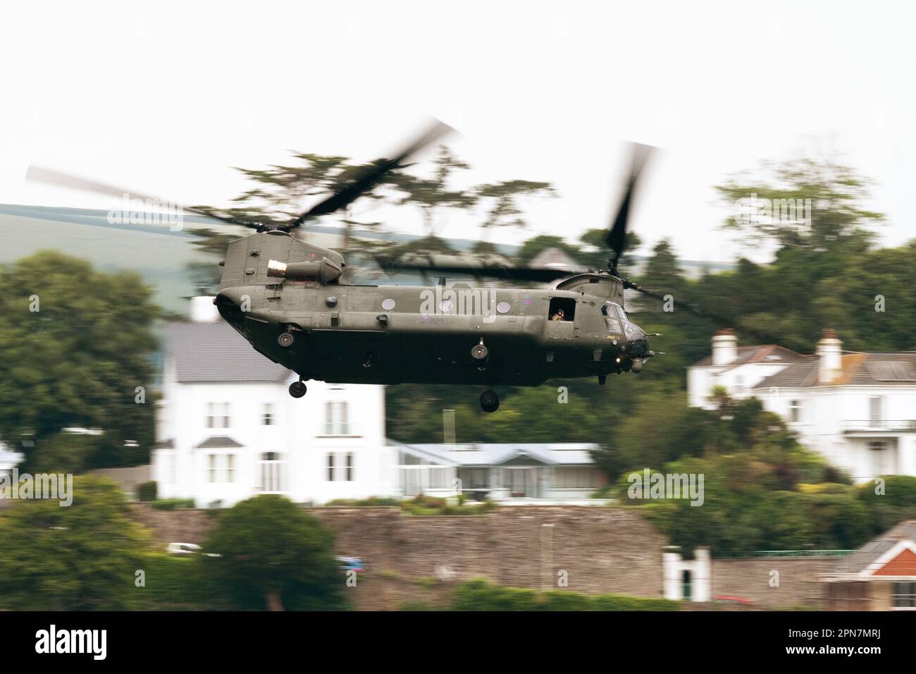 A Royal Air Force Chinook helicopter makes a low pass in front of houses in Kingswear, Devon, UK, June 2020. Photographer: Bryn Colton Stock Photo