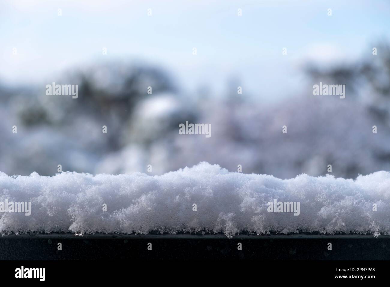 Snow on metal banister on blur nature background. Snowy environment