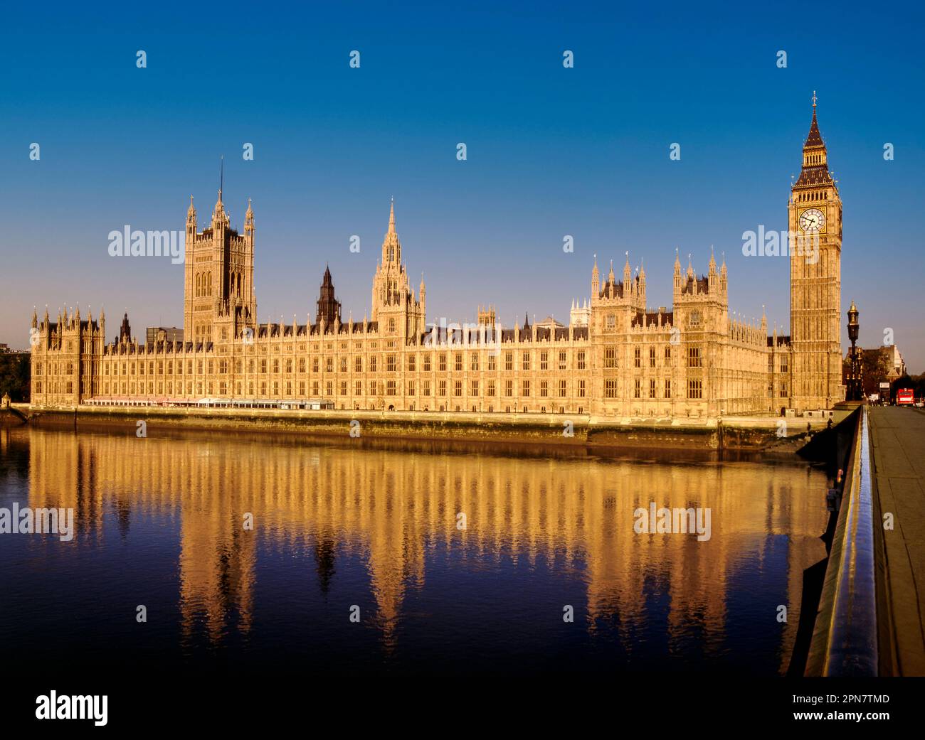Houses of Parliament Westminster Bridge London illuminated by clear dawn sunrise with clear blue sky, reflected in the still River Thames at high tide from Westminster Bridge London UK Stock Photo