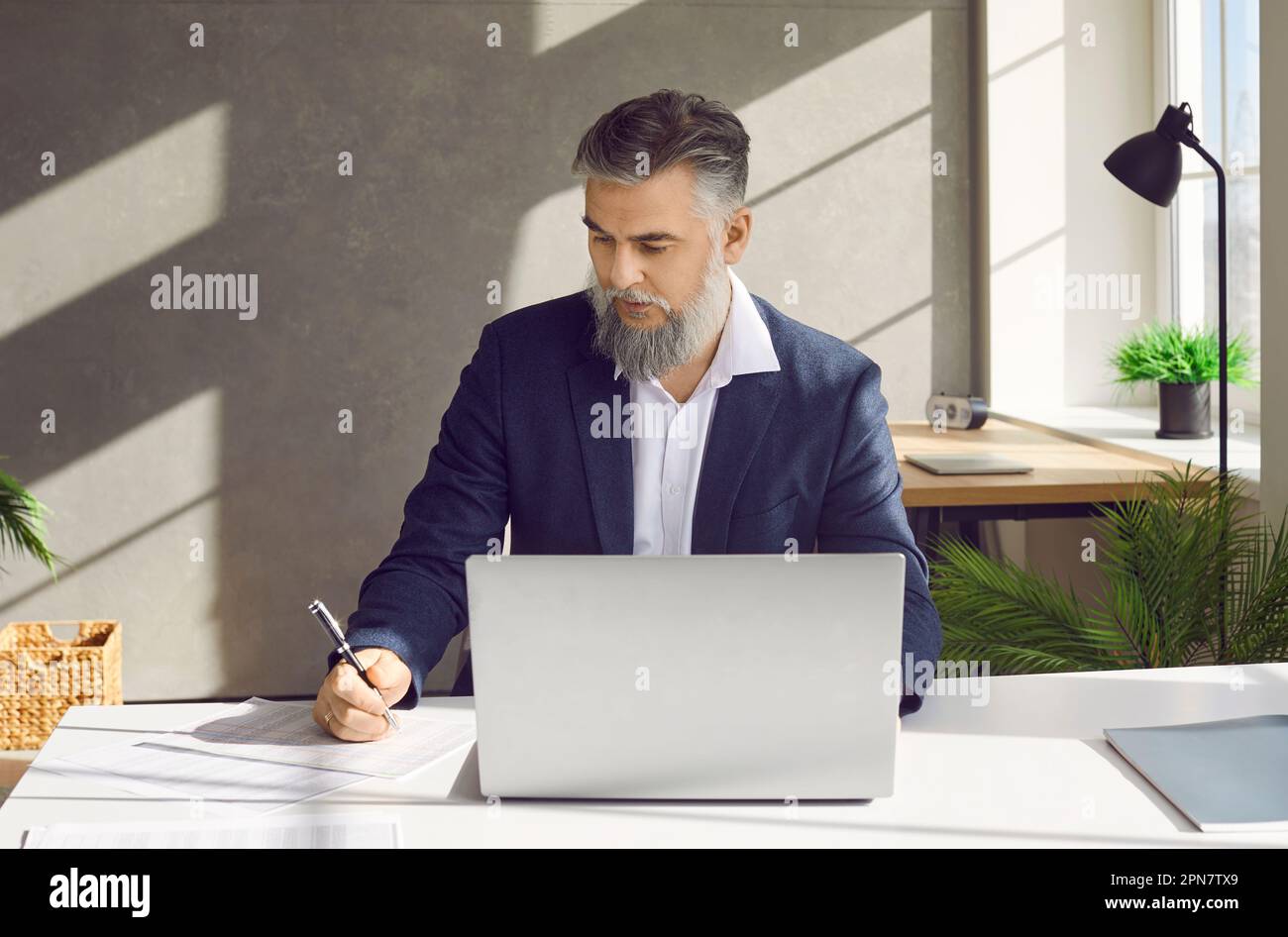 Mature businessman working in the office, using his laptop, and writing something on paper Stock Photo