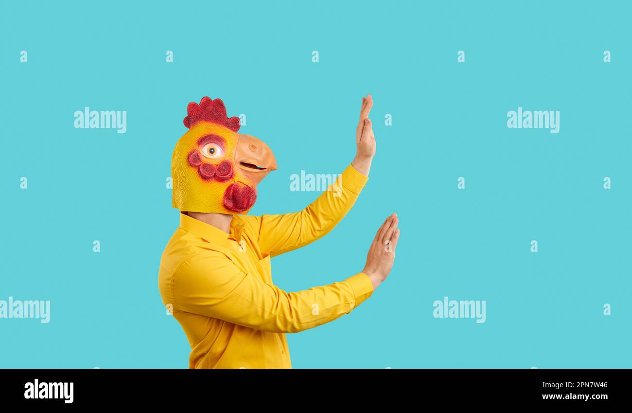 Man in funny chicken mask dancing or pushing invisible wall isolated on turquoise background Stock Photo