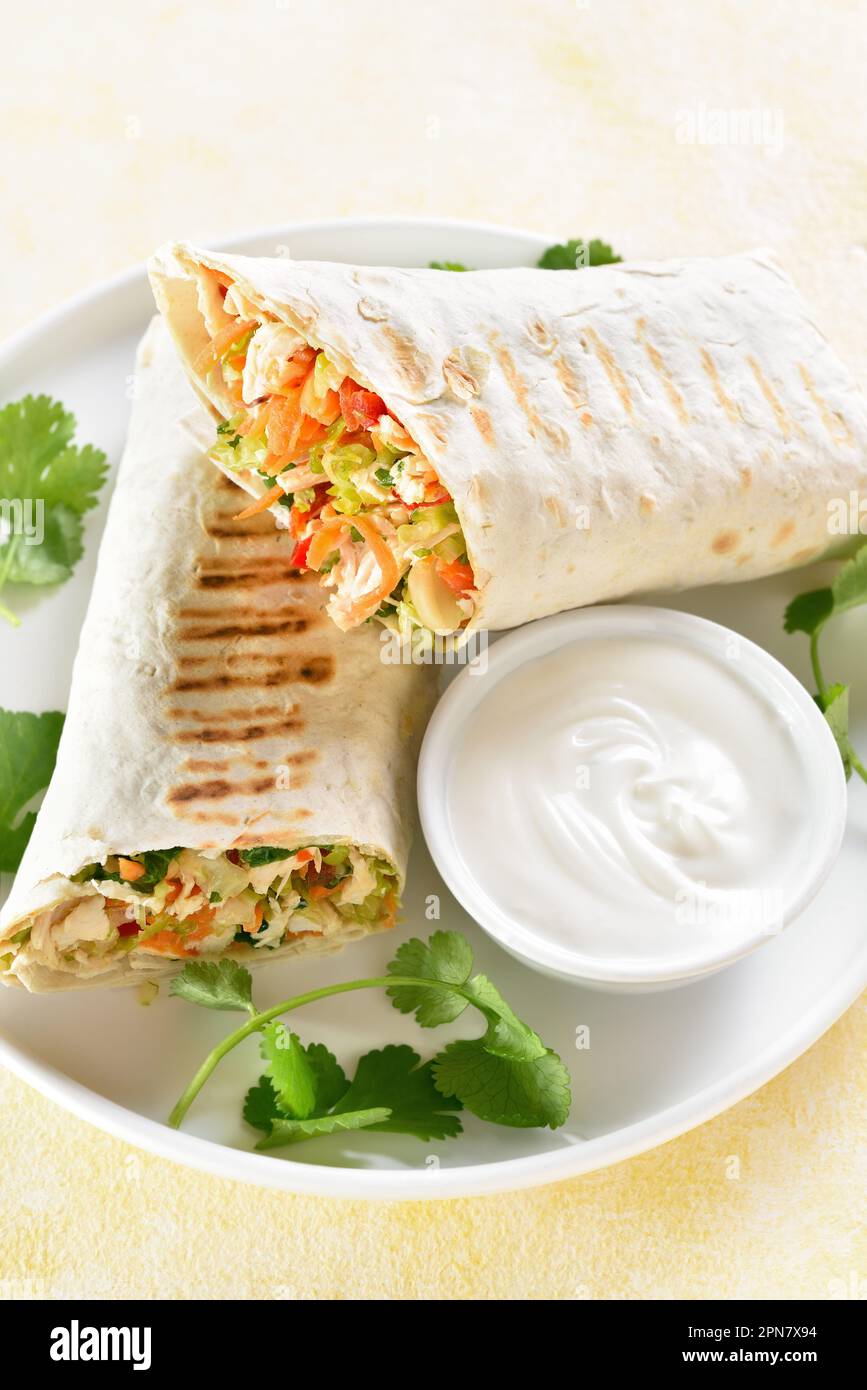 Tortilla wraps with chicken and fresh vegetables on plate over light background. Close up view Stock Photo