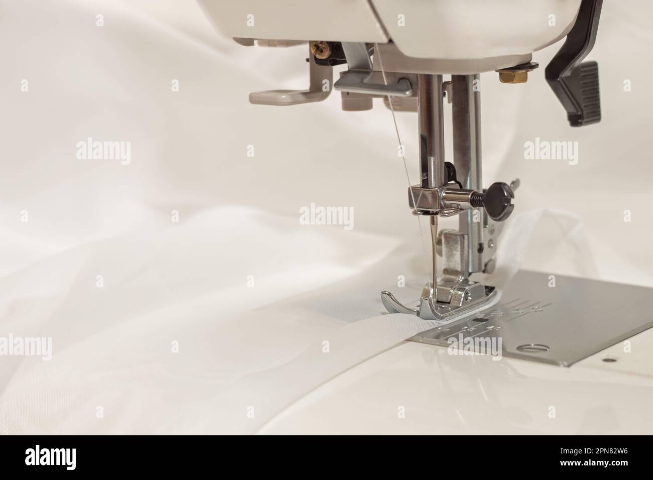 Modern sewing machine presser foot makes a seam on white fabric. Sewing