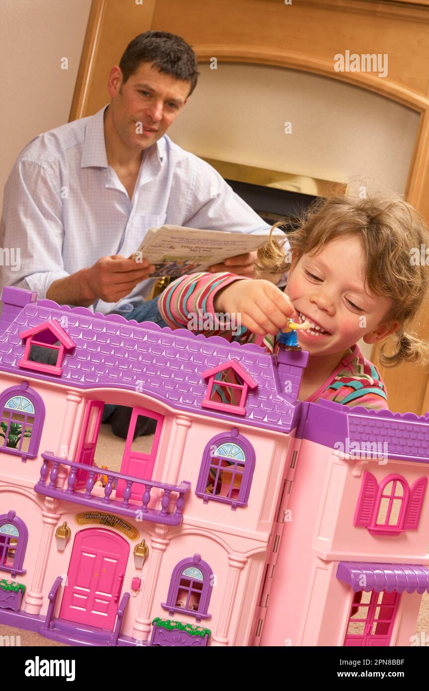 Young girl playing with a pink dolls house with her father in the background Stock Photo