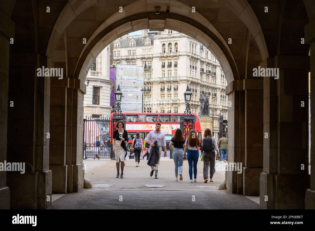 LONDON - May 18, 2022: A busy London scene as people walk through the entrance arch to Horse Guards Parade, with the iconic red double-decker bus in t Stock Photo