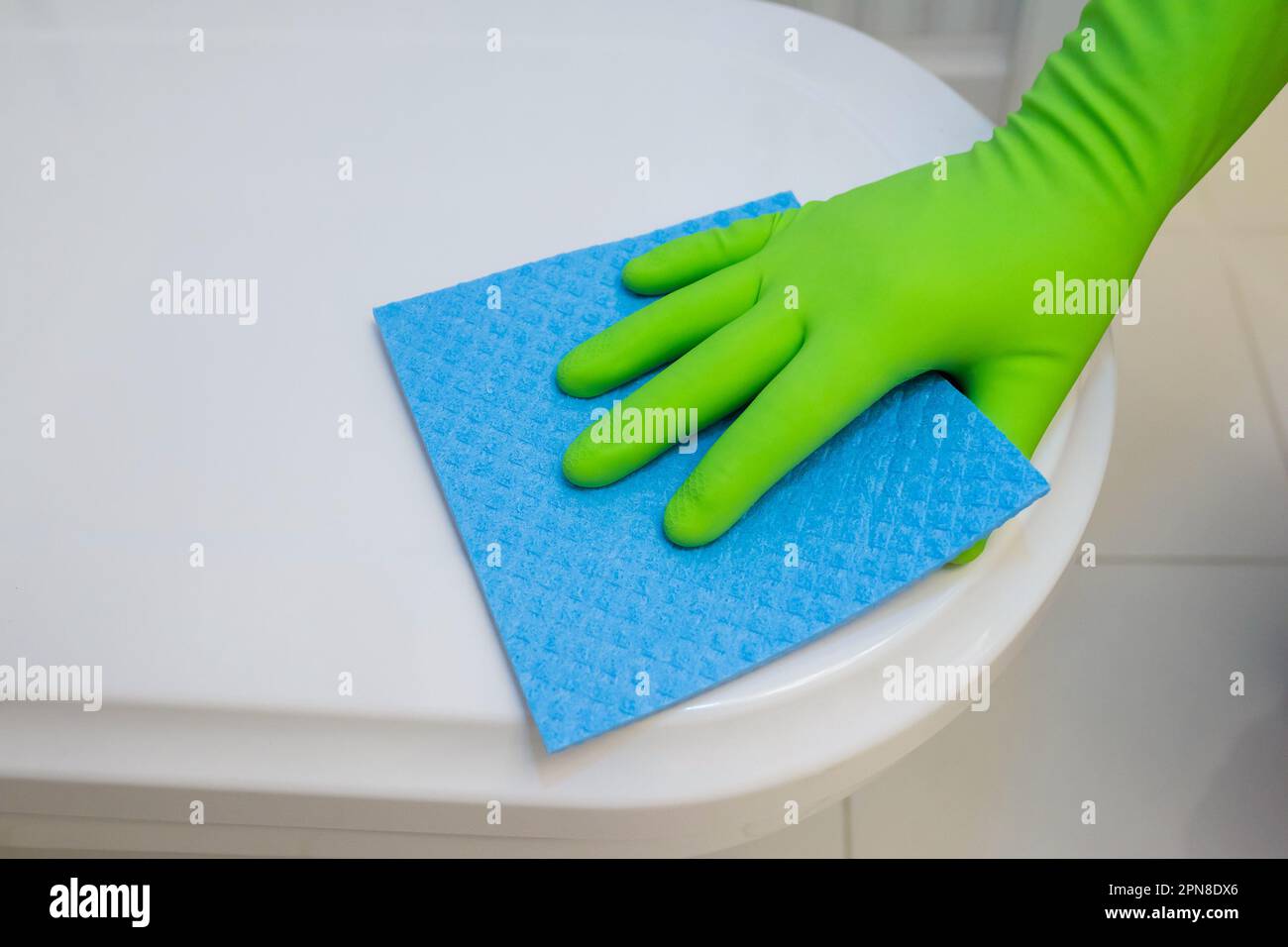 Woman in green rubber gloves cleaning toilet seat with blue cloth. Bathroom and toilet hygiene
