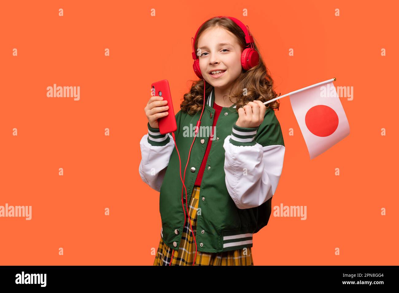 Teen school girl in casual clothes and headphones holds small national flag of Japan and