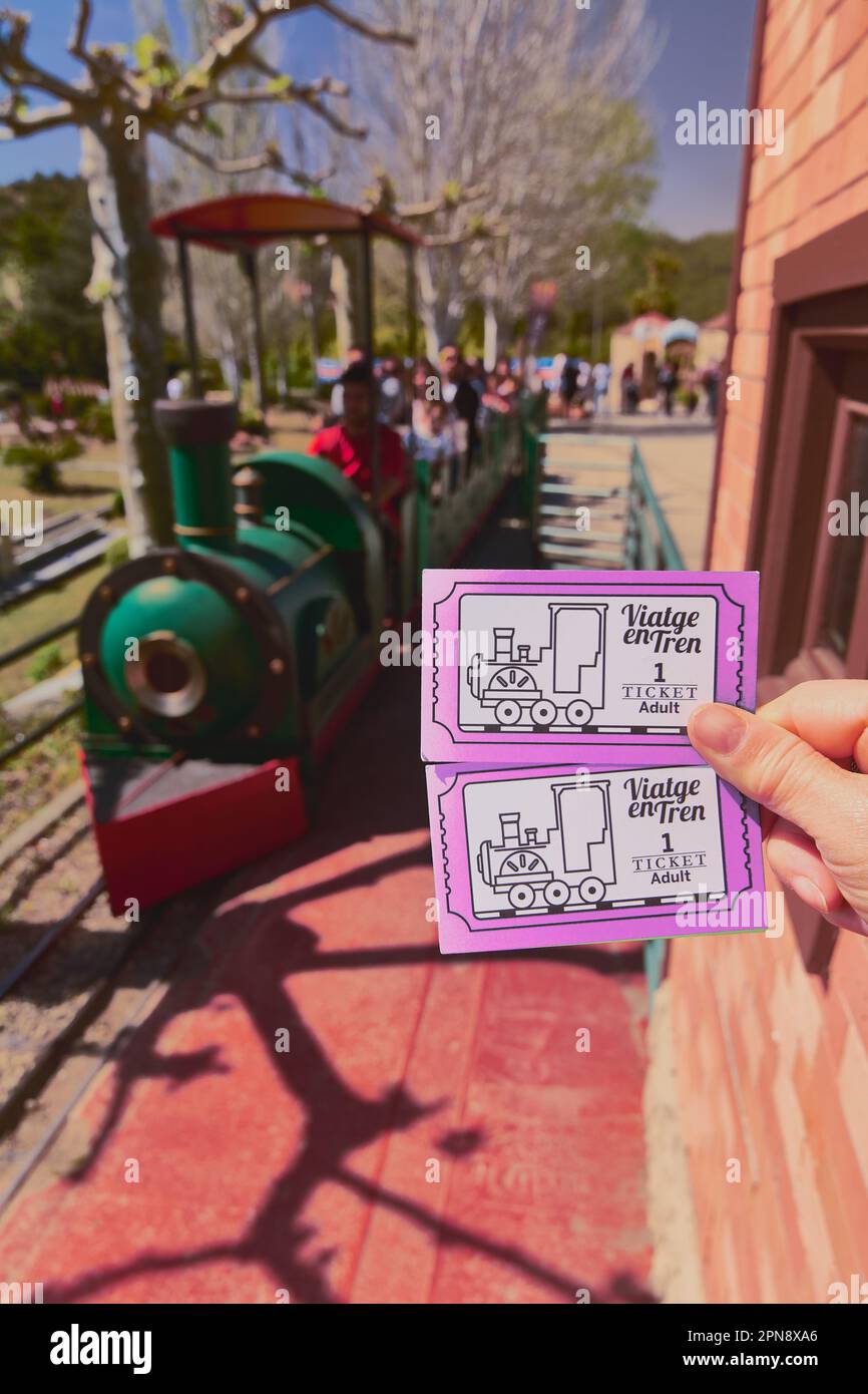 Concept exploring the thrill of travel: hand holding miniature Catalunya train tickets, while the train carriages fade into the blurred background Stock Photo