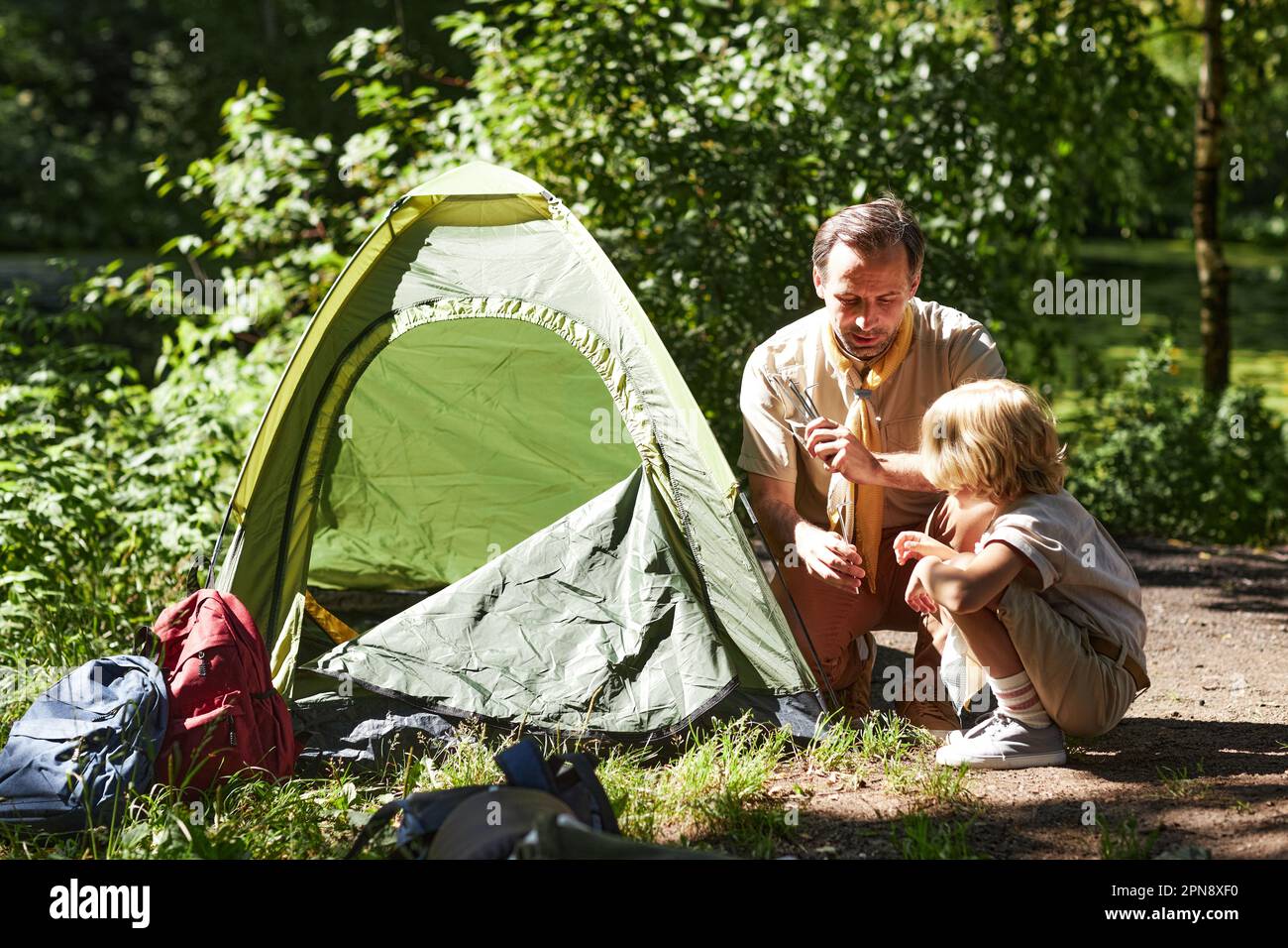 Portrait of adult man as scout leader teaching little boy how to set tents in forest Stock Photo