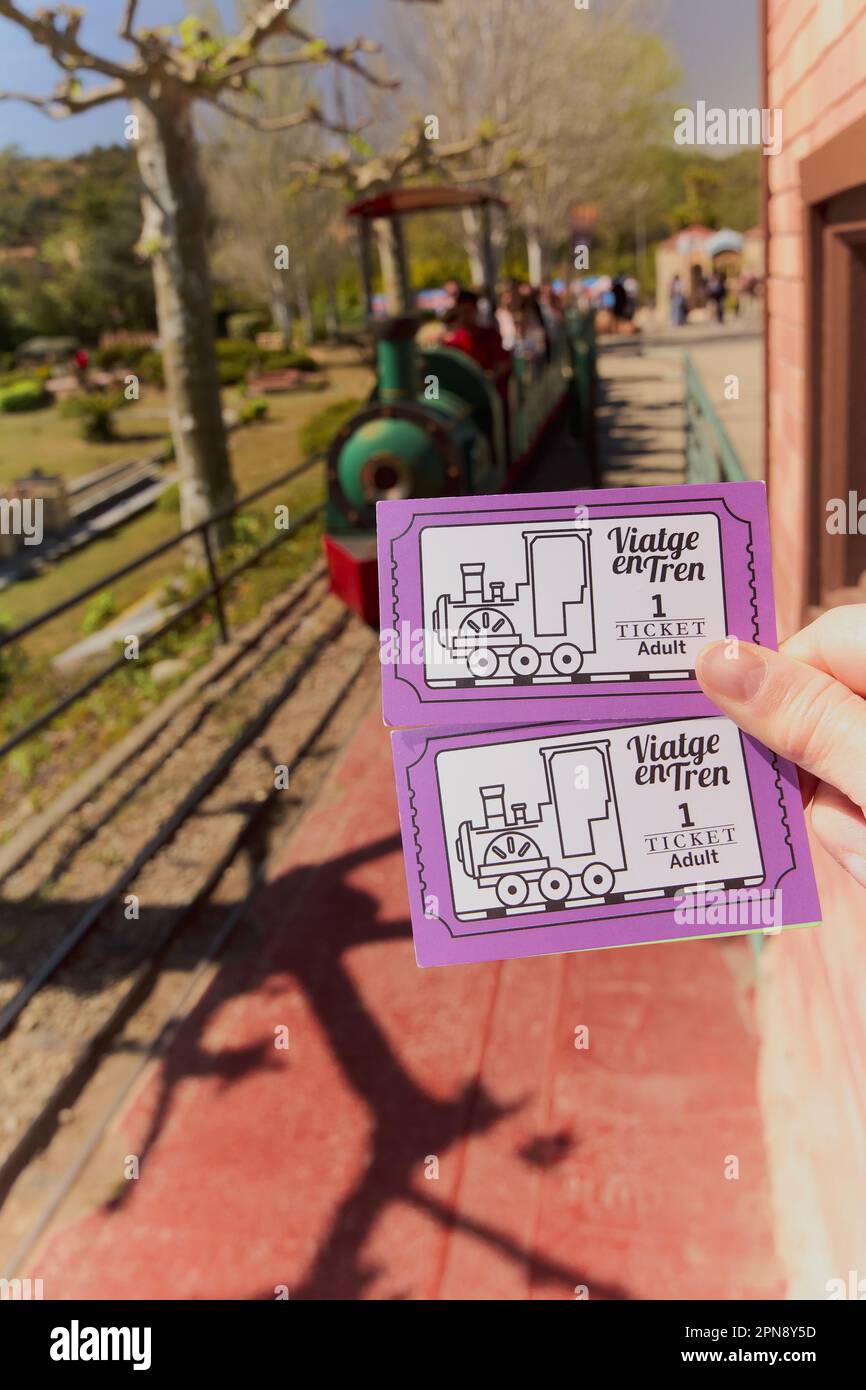 Concept exploring the thrill of travel: hand holding miniature Catalunya train tickets, while the train carriages fade into the blurred background Stock Photo