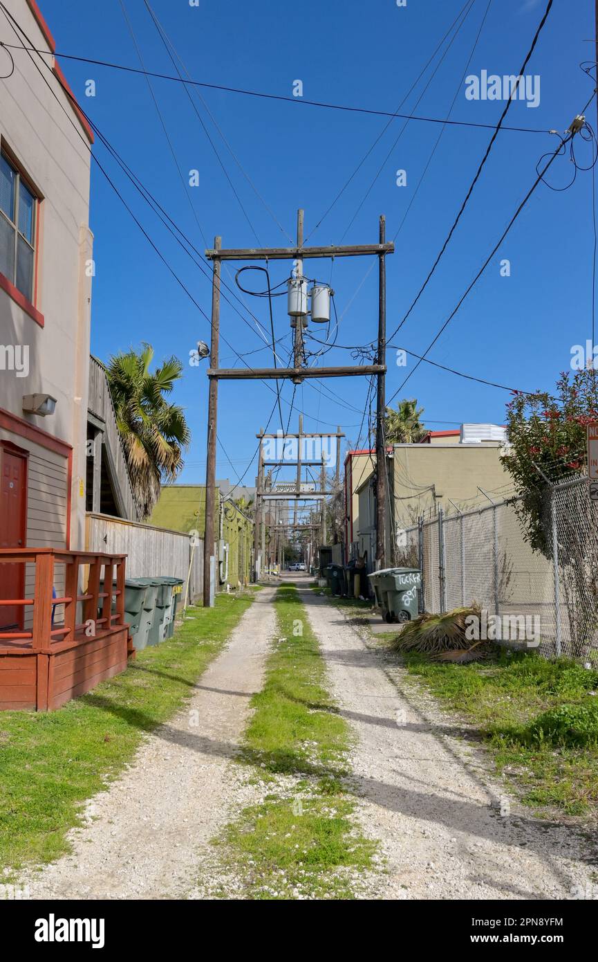 Galveston, Texas, USA - February 2023: Unpaved lane with power lines running between the backs of buildings near the city centre Stock Photo