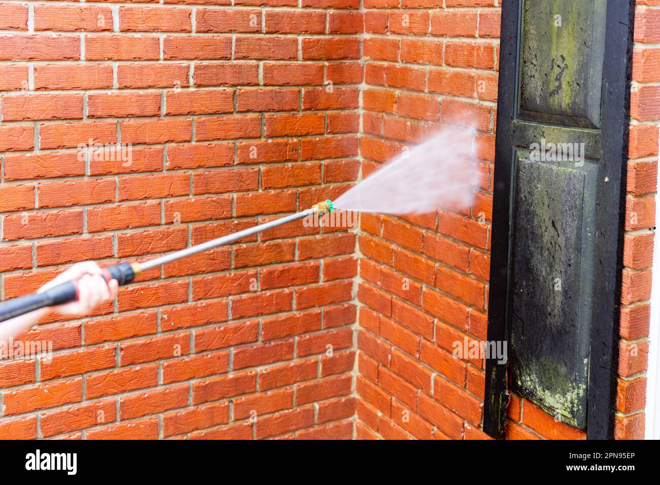 Brick wall being cleaned with water from pressure washer Stock Photo