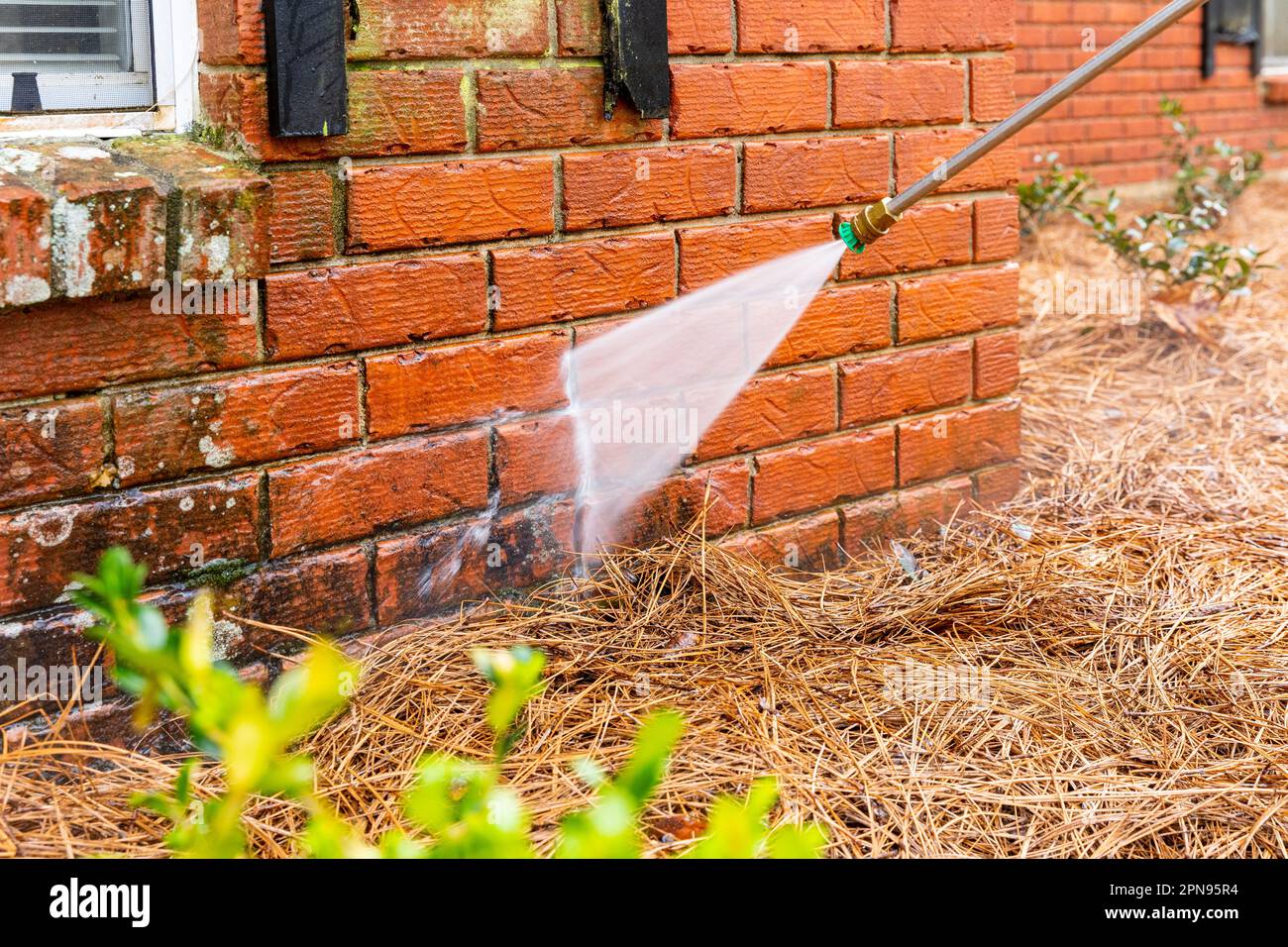 Pressure washer using water to clean a dirty brick wall on a house