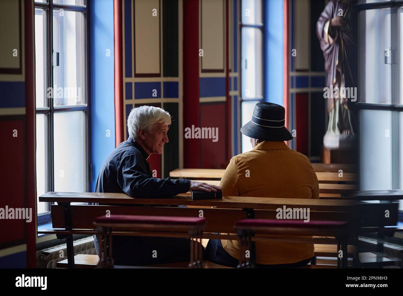 Rear view of senior priest talking to visitor while they sitting on bench during ministration in church Stock Photo