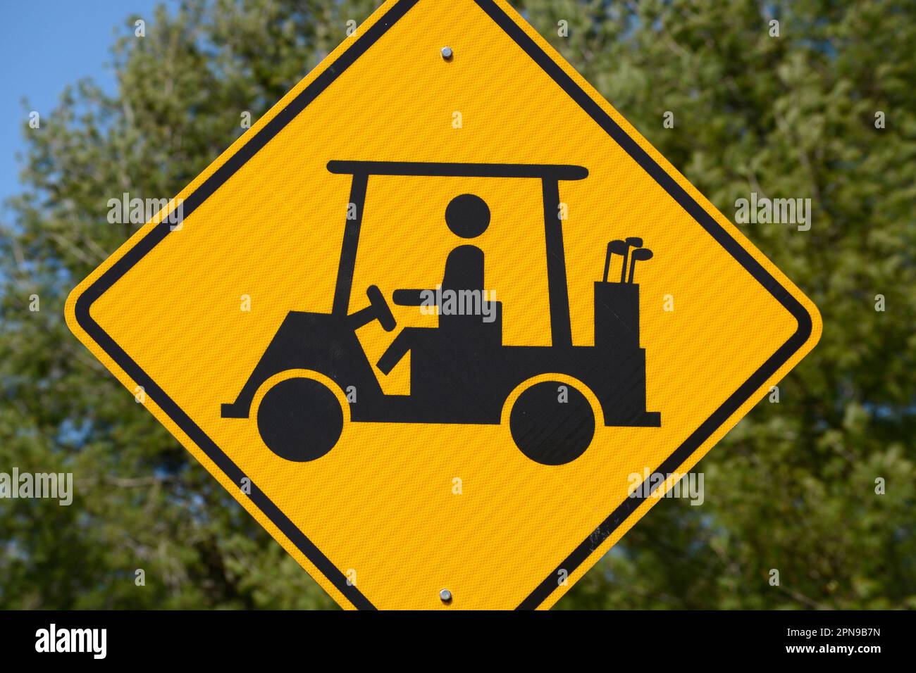 A golf cart crossing sign along a road warns motorists to watch for