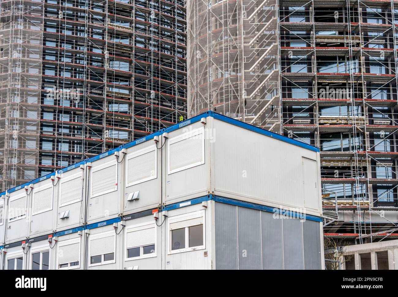 Large construction site, construction of a high-rise residential building, scaffolded shell, already fitted with windows, in front of it containers fo Stock Photo