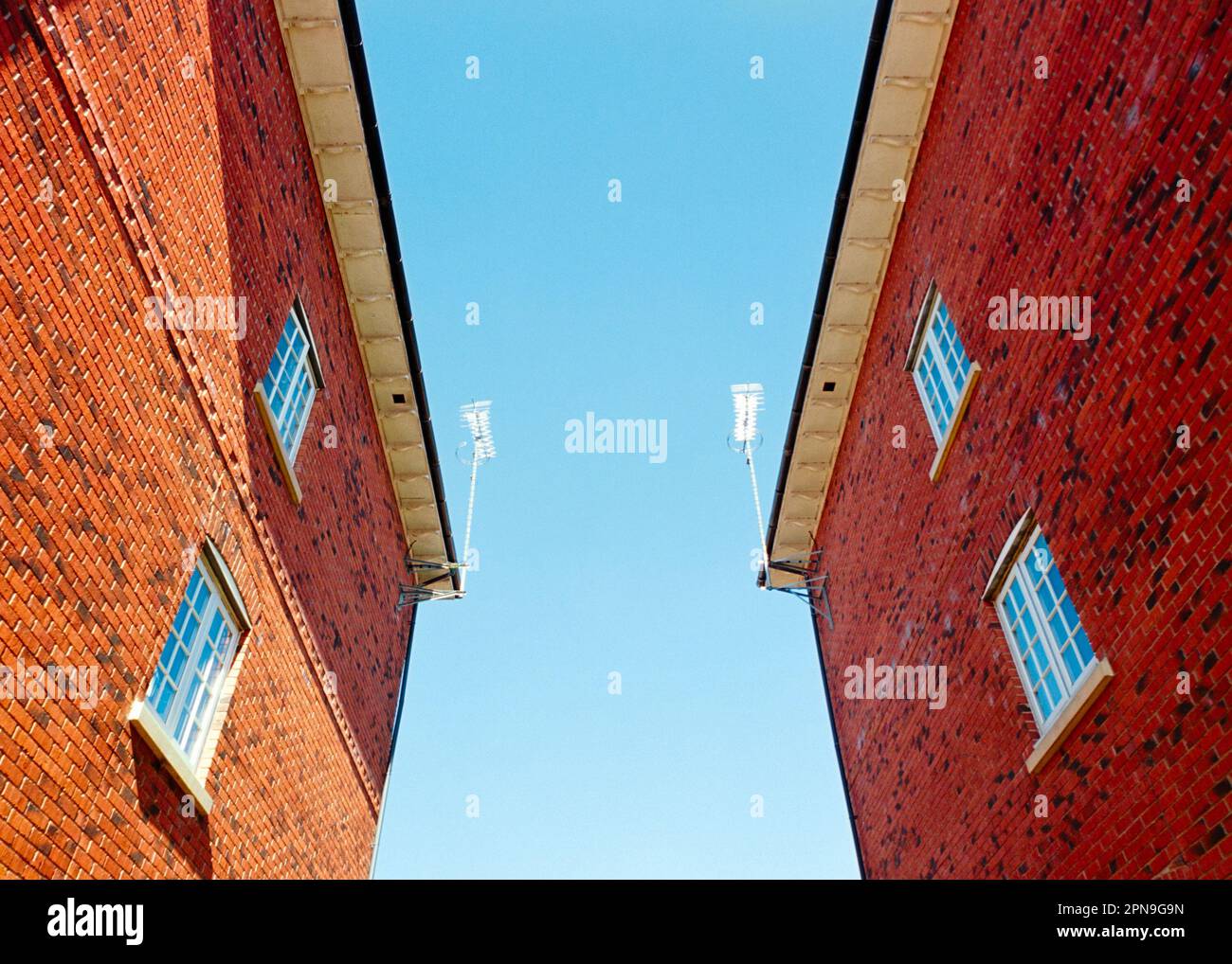 Blue sky viewed from in between two red brick residential buildings or flats/apartments. Blank space for copy or content insertion Stock Photo