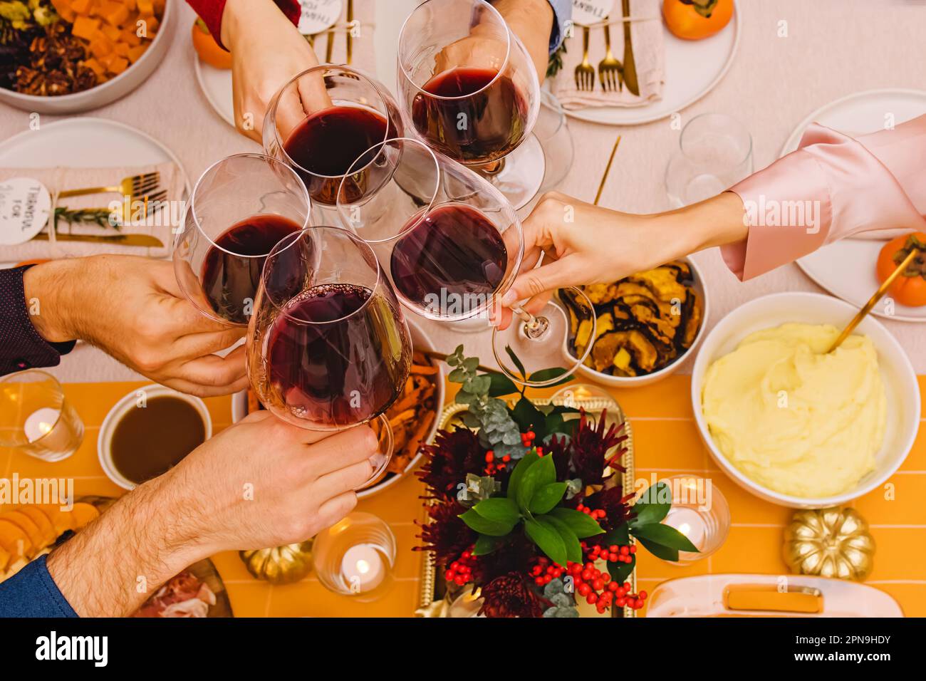Unrecognizable people clinking with a glasses filled with red wine sitting at the Thanksgiving dinner table. Celebration, gather, Friendsgiving Stock Photo