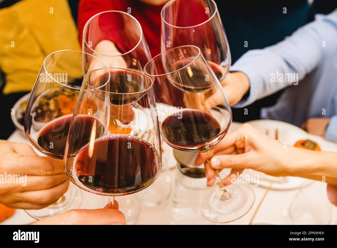 Hands clinking with a glasses filled with red wine sitting at the Thanksgiving dinner table. Celebration, gather, Friendsgiving Stock Photo