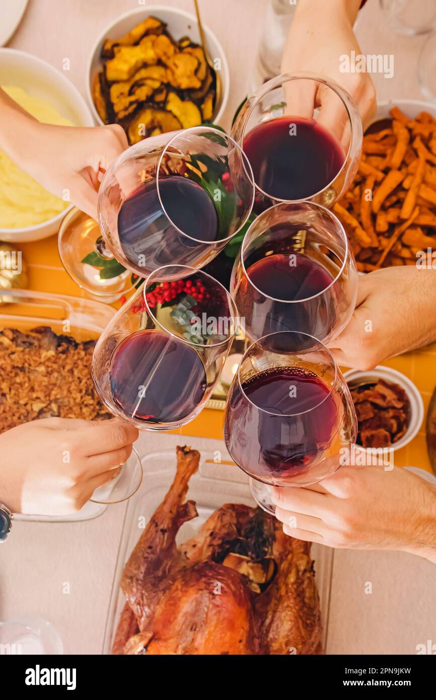 Thanksgiving or Friendsgiving dinner, hand holding glasses with red wine, celebrating Stock Photo