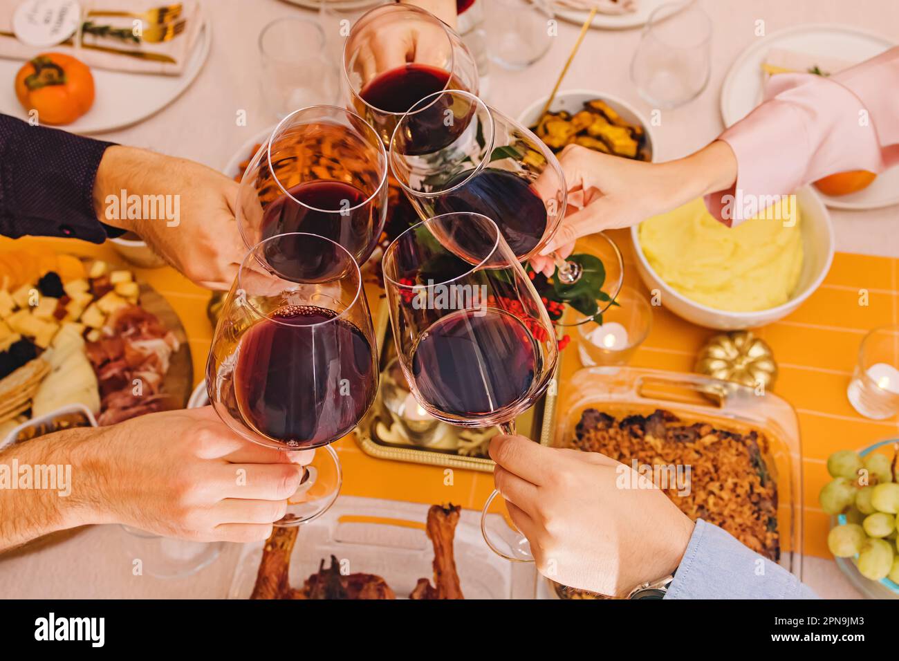 Hands clinking with a glasses filled with red wine at the Thanksgiving dinner table. Celebration, gather, Friendsgiving Stock Photo