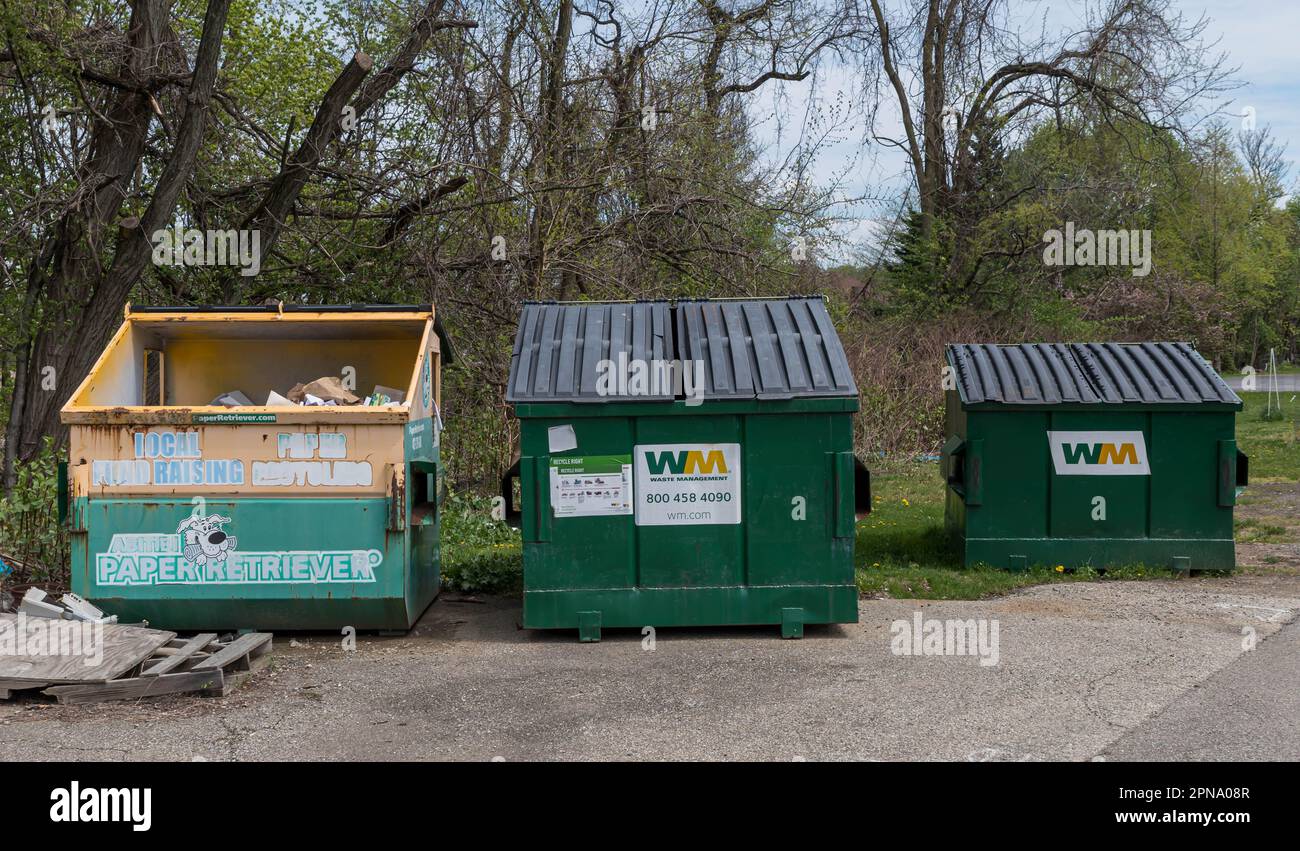 Two Waste Management garbage dumpsters and a paper recycling bin in a