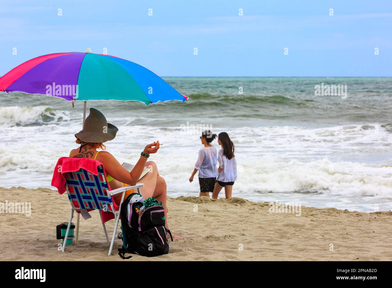 A colorful umbrella shades a woman relaxing surfside under while