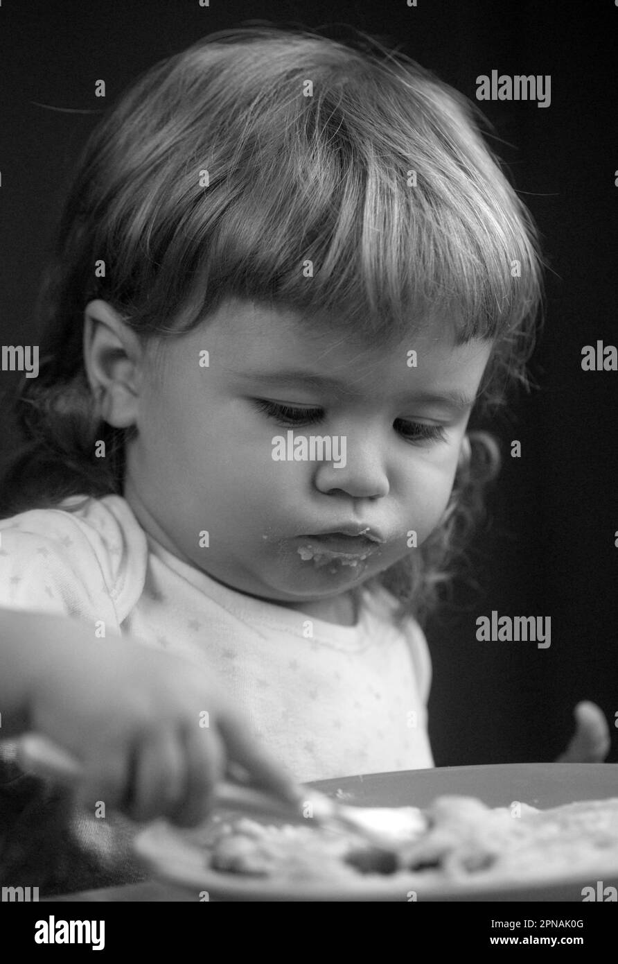 Kid baby with a spoon and a plate in the kitchen at home Stock Photo
