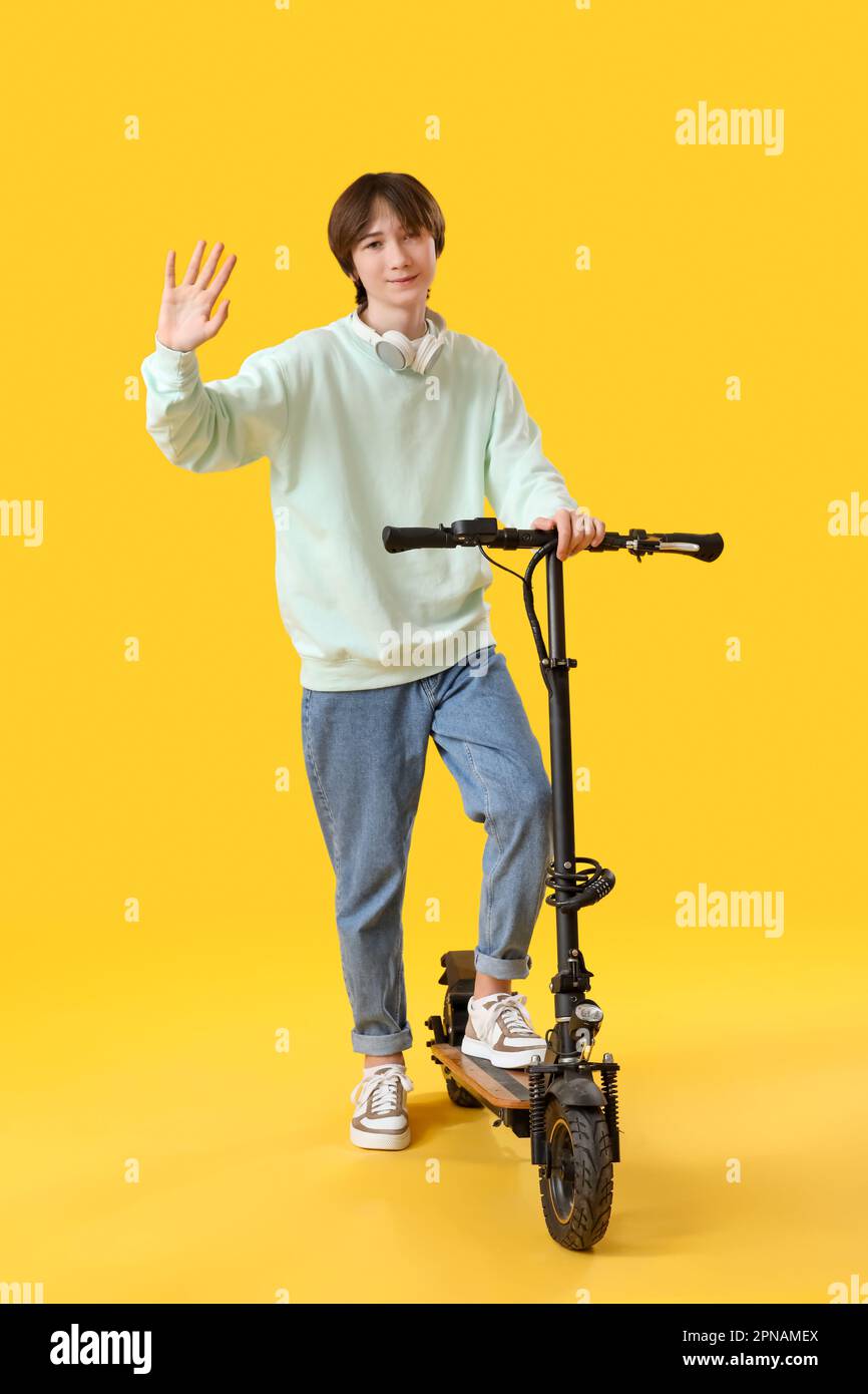 Teenage boy with electric bike waving hand on yellow background Stock