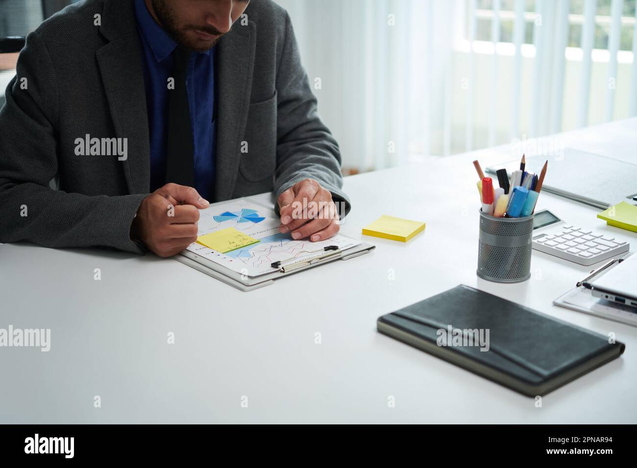 Serious entrepreneur analyzing chart and taking notes on yellow sticker Stock Photo