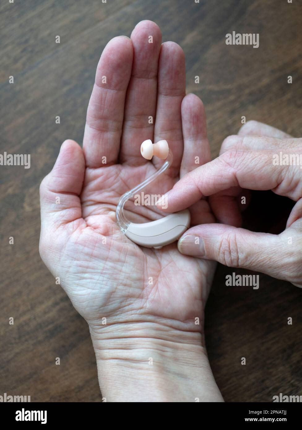 Hearing aid in hand, vertical format. Assistive listening or alerting devices. World hearing day Stock Photo