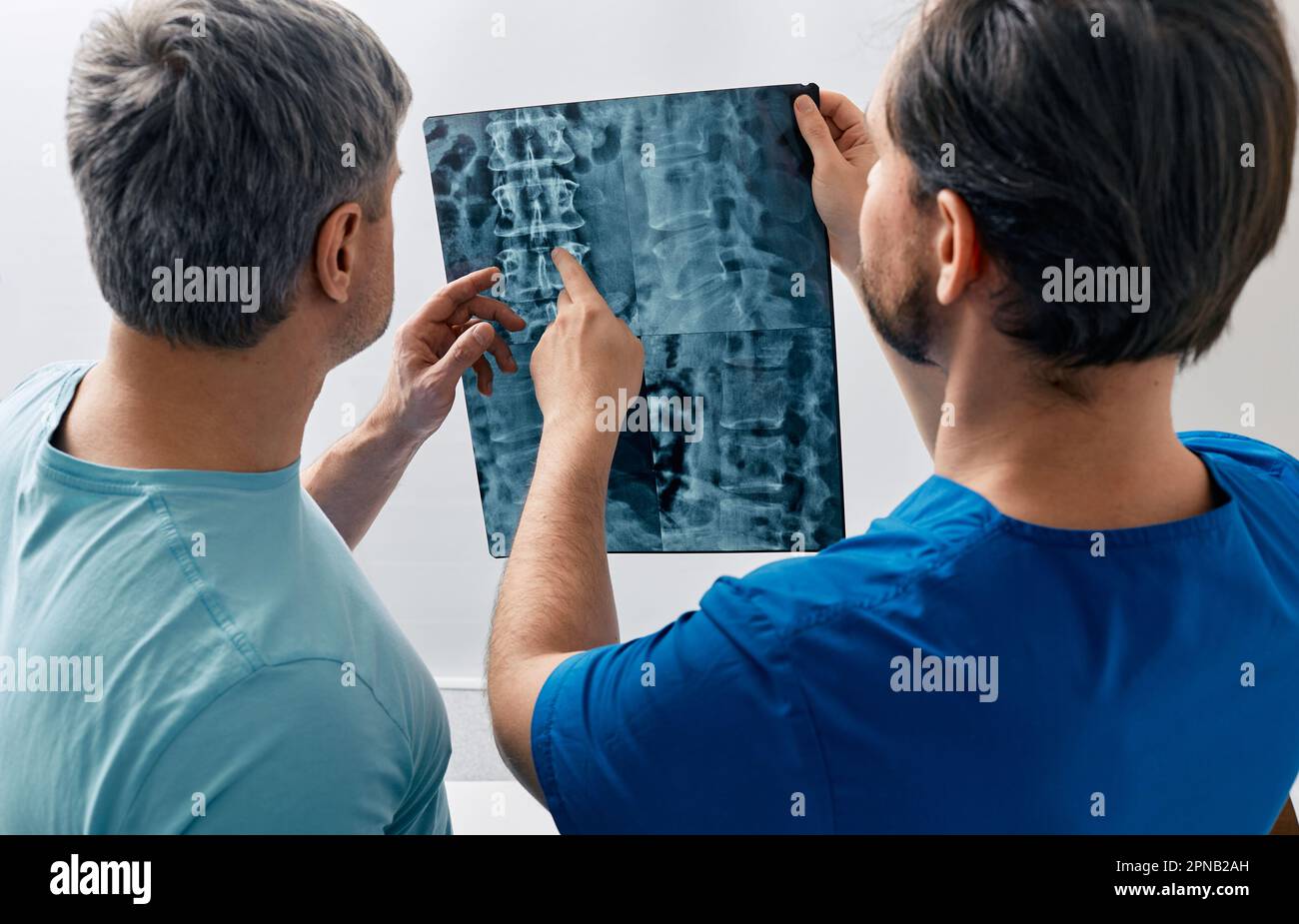 Manual therapist viewing X-ray of backbone with his male patient with spinal problem during medical consultation at hospital Stock Photo