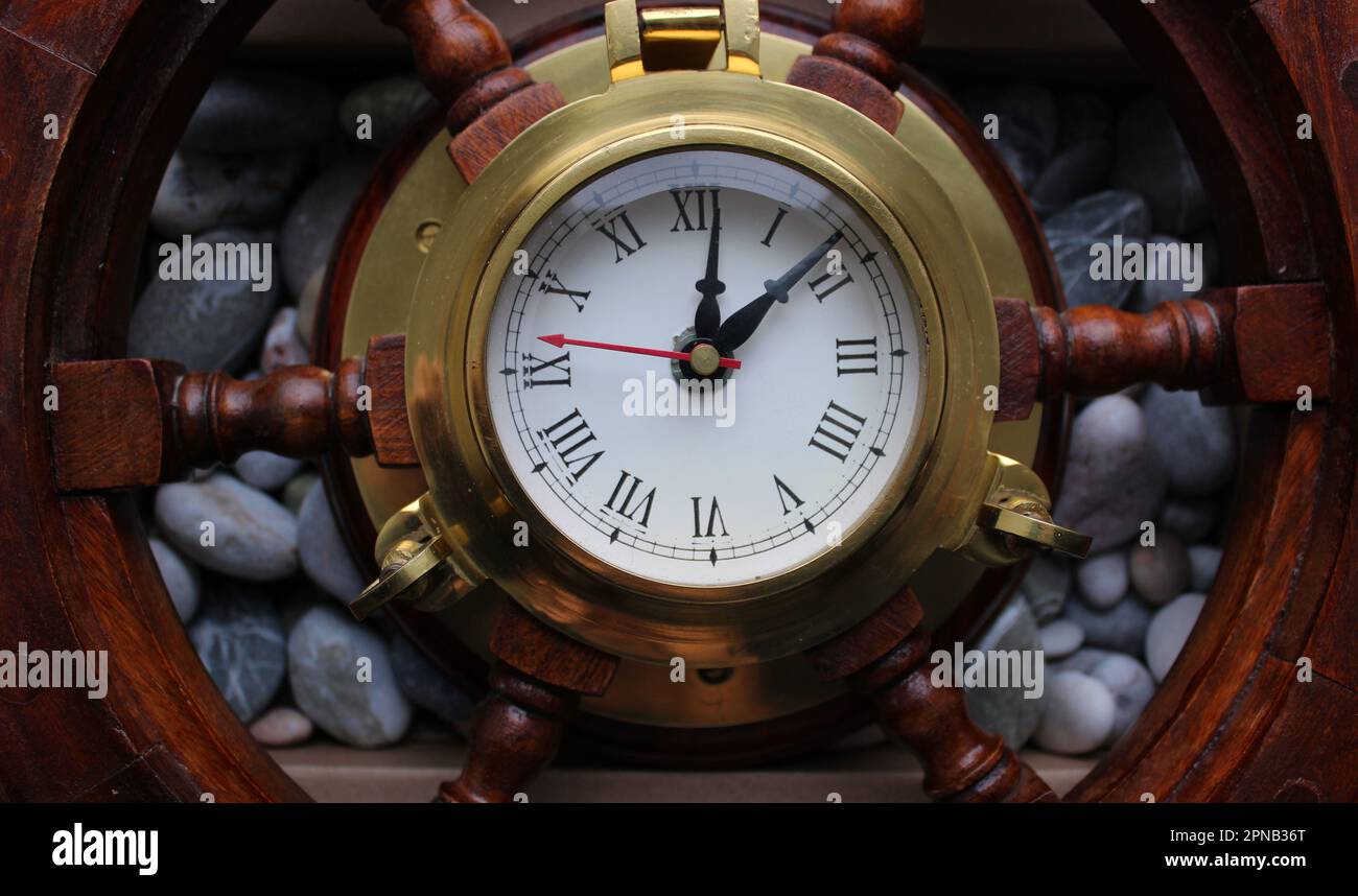 Pointer Clock With Copper Frame In A Center Of Wooden Helm On A Sea Pebbles Background Stock Photo