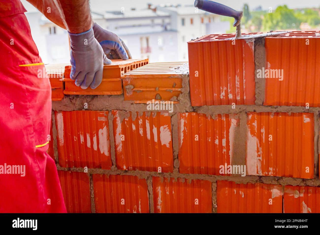 Mason, bricklayer worker is using red blocks to mount a wall next the