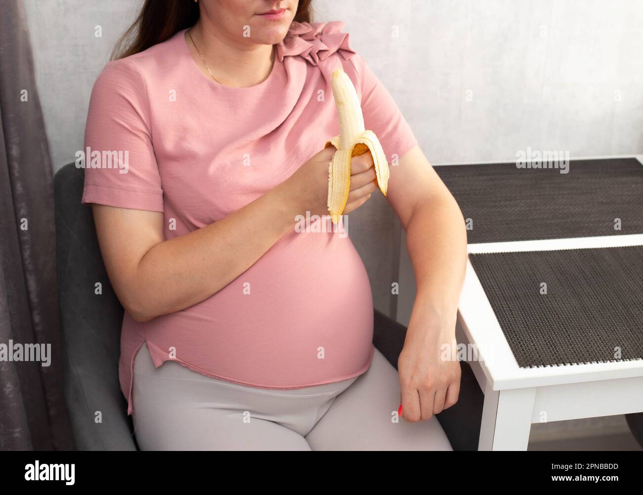 A pregnant girl eats a banana in the kitchen. The concept of healthy eating vegetables and