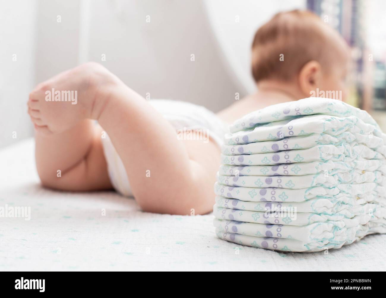 The legs of a baby in a diaper against the background of a stack of