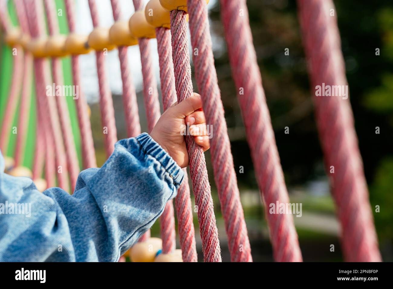 Anonymous little boy in jeans jacket holding rope while spending time ...
