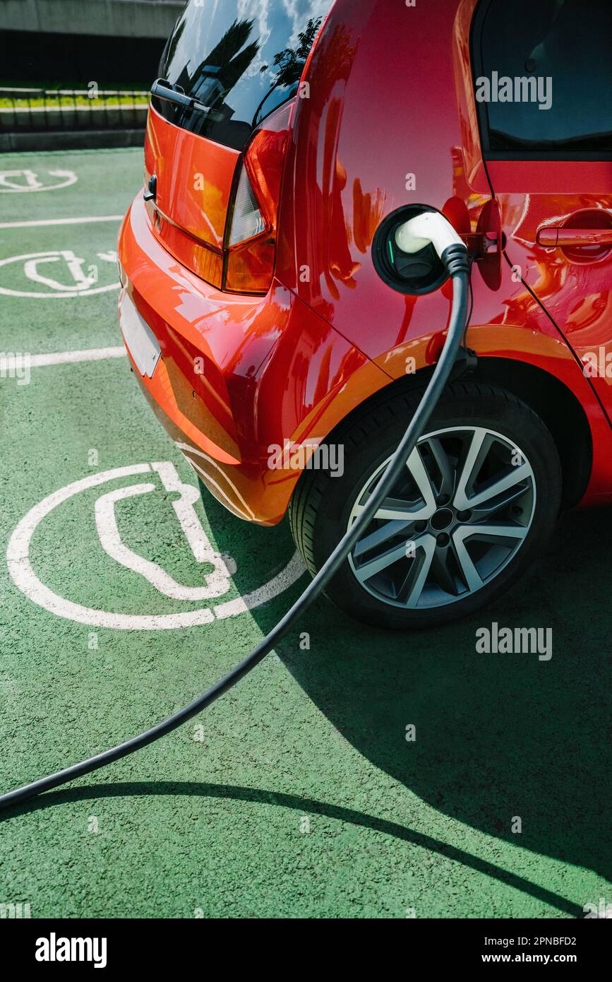 Contemporary red electric car parked on asphalt road while charging