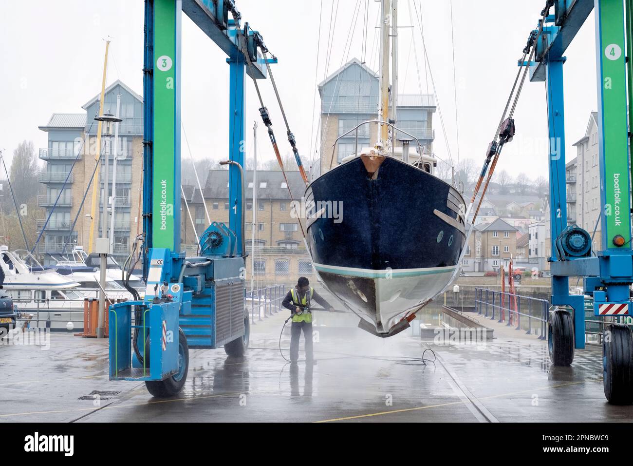 A female boat yard maintenance operator cleans the hull of a boat lifted from the water in Portishead Marina UK. the boat is held in a Wise Boat Hoist Stock Photo