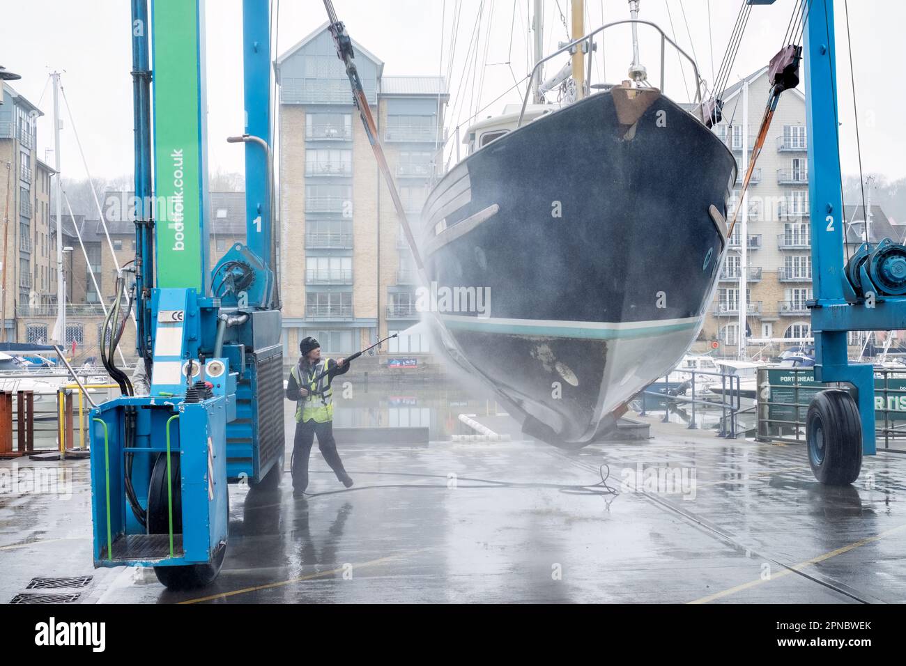 A female boat yard maintenance operator cleans the hull of a boat lifted from the water in Portishead Marina UK. the boat is held in a Wise Boat Hoist Stock Photo