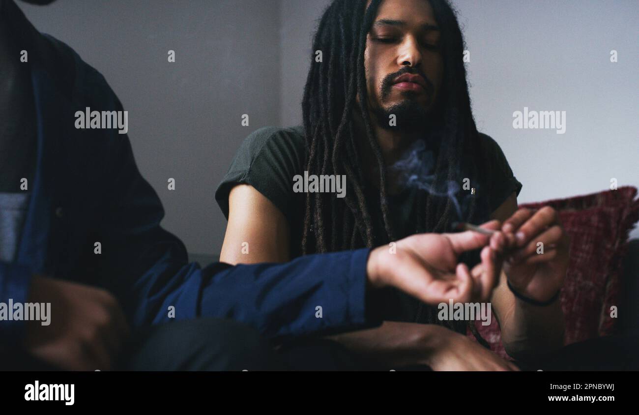 Puff, puff, pass. two young men smoking a marijuana joint at home Stock