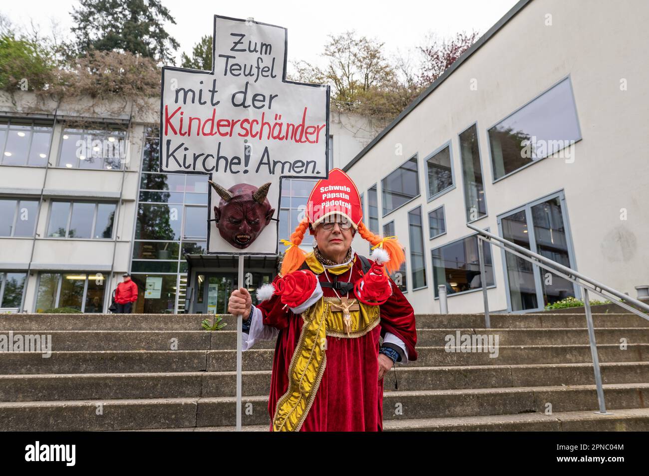 Freiburg Im Breisgau, Germany. 18th Apr, 2023. A man holds a sign outside the Catholic Academy before the start of a press conference by the Archdiocese of Freiburg on dealing with abuse that reads 'To hell with the child molester church! Amen.' The report on the previous handling of sexualized violence was compiled by independent experts. Credit: Silas Stein/dpa/Alamy Live News Stock Photo