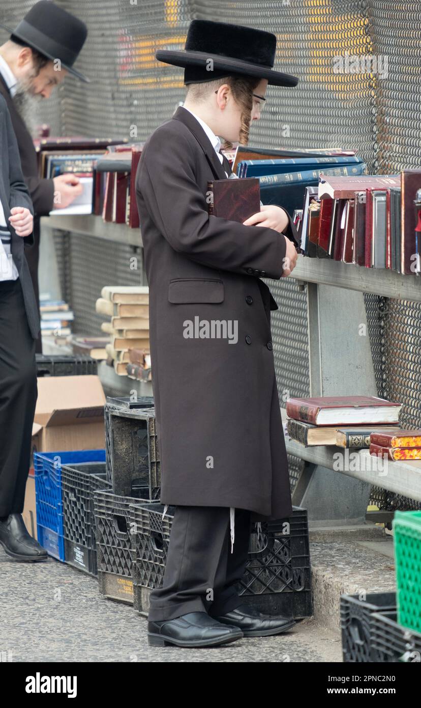 A young orthodox Jewish lad with long curly peyus shops for religious books at a pop up outdoor sale in Williamsburg, Brooklyn, New York City. Stock Photo
