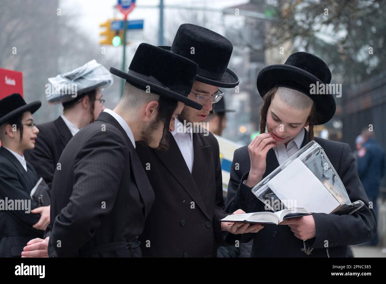 3 Hasidic jewish men share a prayer book at the ceremony for burning